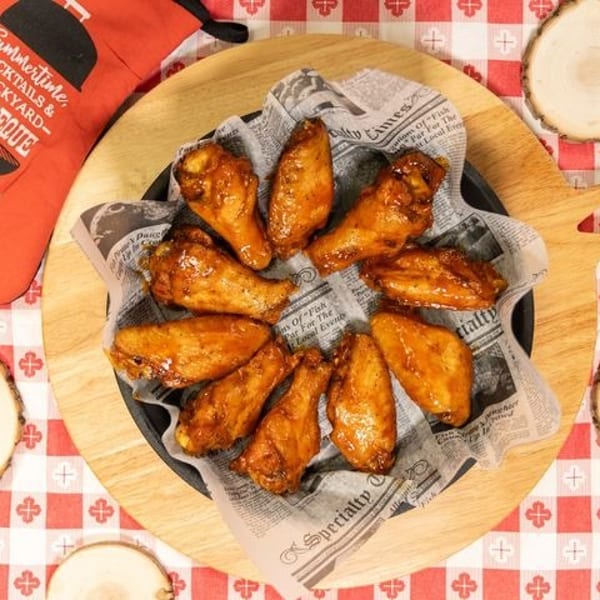 Glazed chicken wings in a skillet lined with newspaper, on a red and white checkered tablecloth.